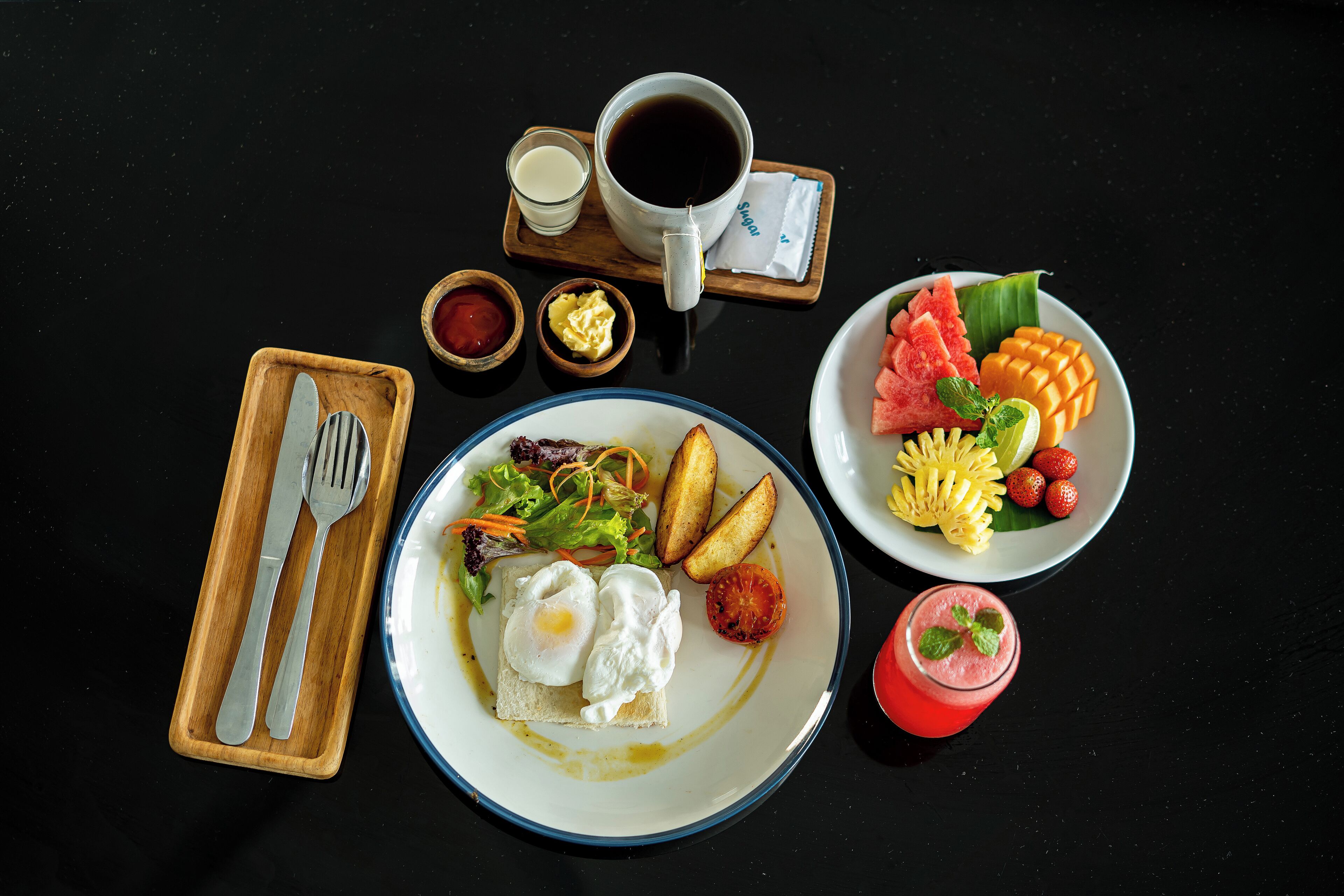 Un desayuno con huevos, tostadas, verduras, una taza de café y un bol de fruta.