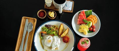 Un desayuno con huevos, tostadas, verduras, una taza de café y un bol de fruta.
