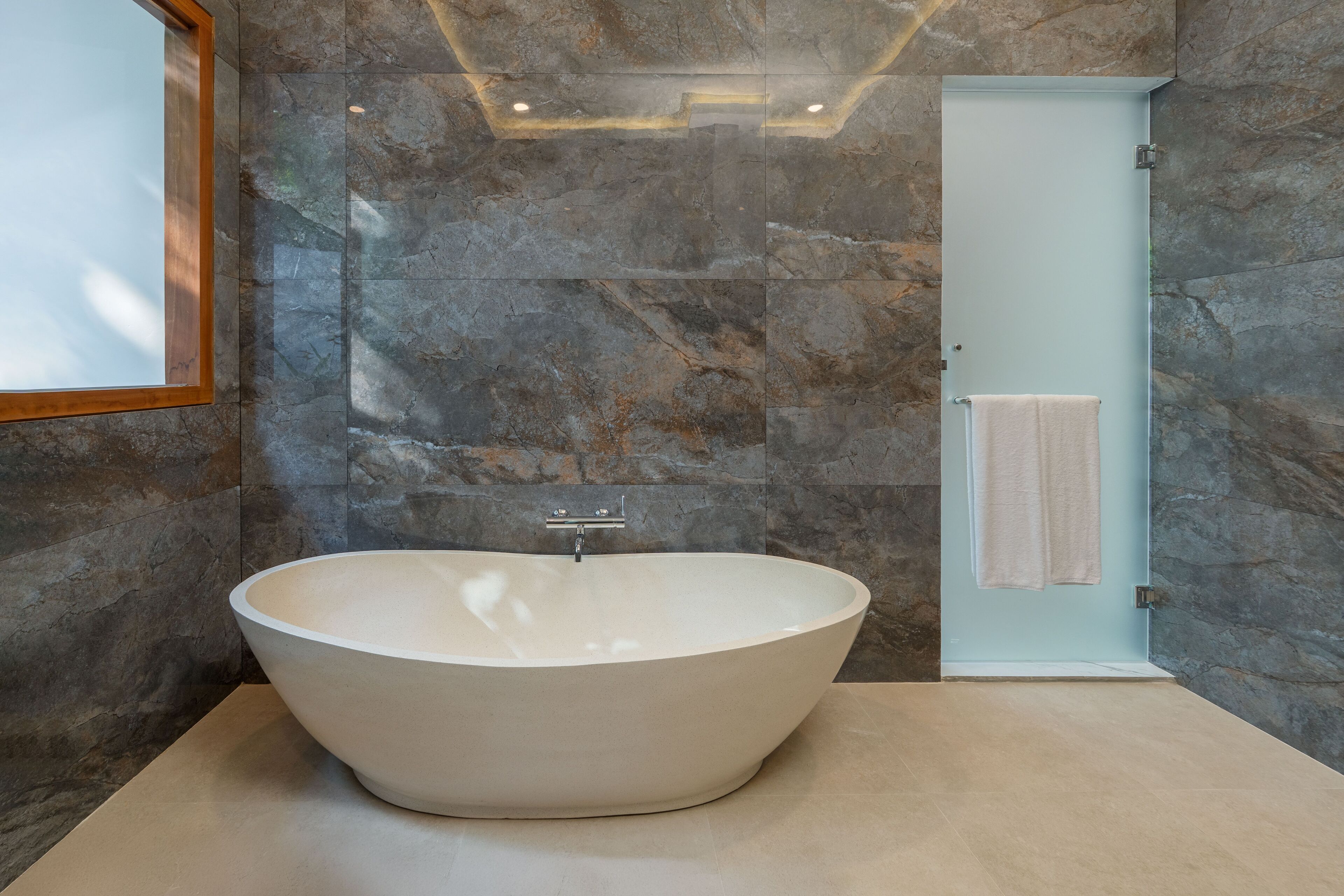 A modern bathroom with a freestanding bathtub, stone walls, and a light blue door.