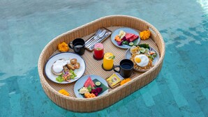 Una disposición para comer flotante, con platos de comida, bebidas y utensilios sobre una superficie de agua azul transparente.