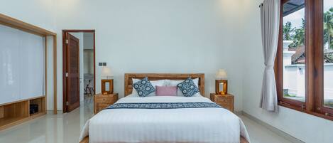 A bedroom with a large bed, wooden headboard, bedside lamps, and a view of the outside.