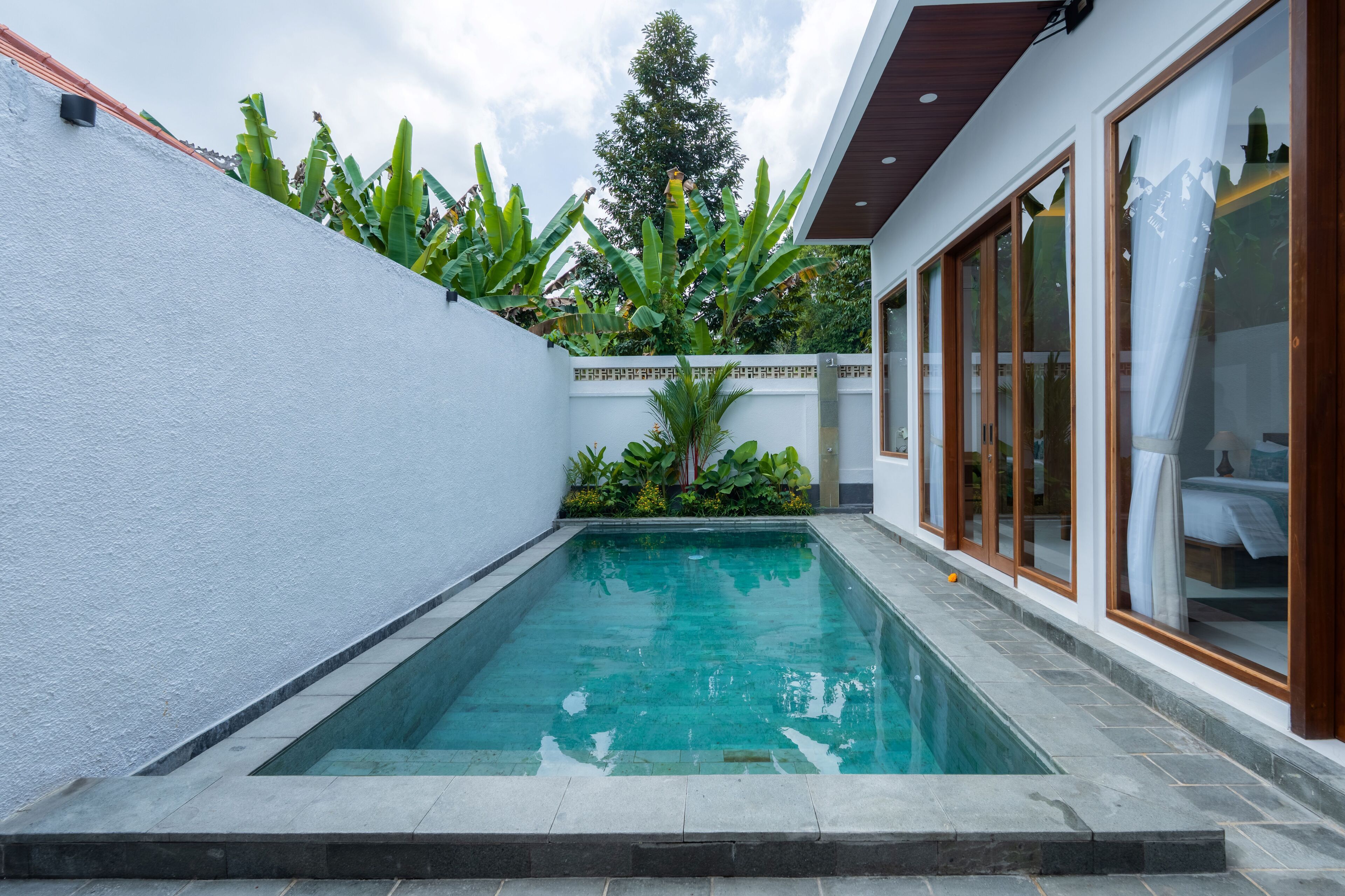 Une piscine rectangulaire à l’eau claire, entourée d’un mur blanc et d’une terrasse en bois.