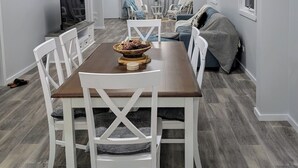 A dining area with a wooden table and white chairs, a ceiling fan, and artwork on the walls.