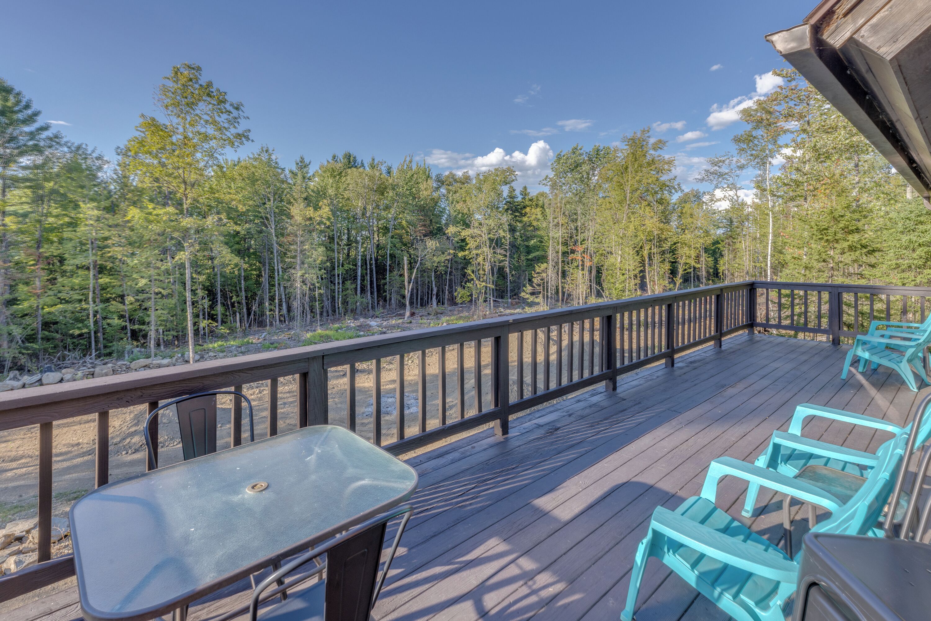 A wooden deck with a table and chairs, overlooking a forested area.
