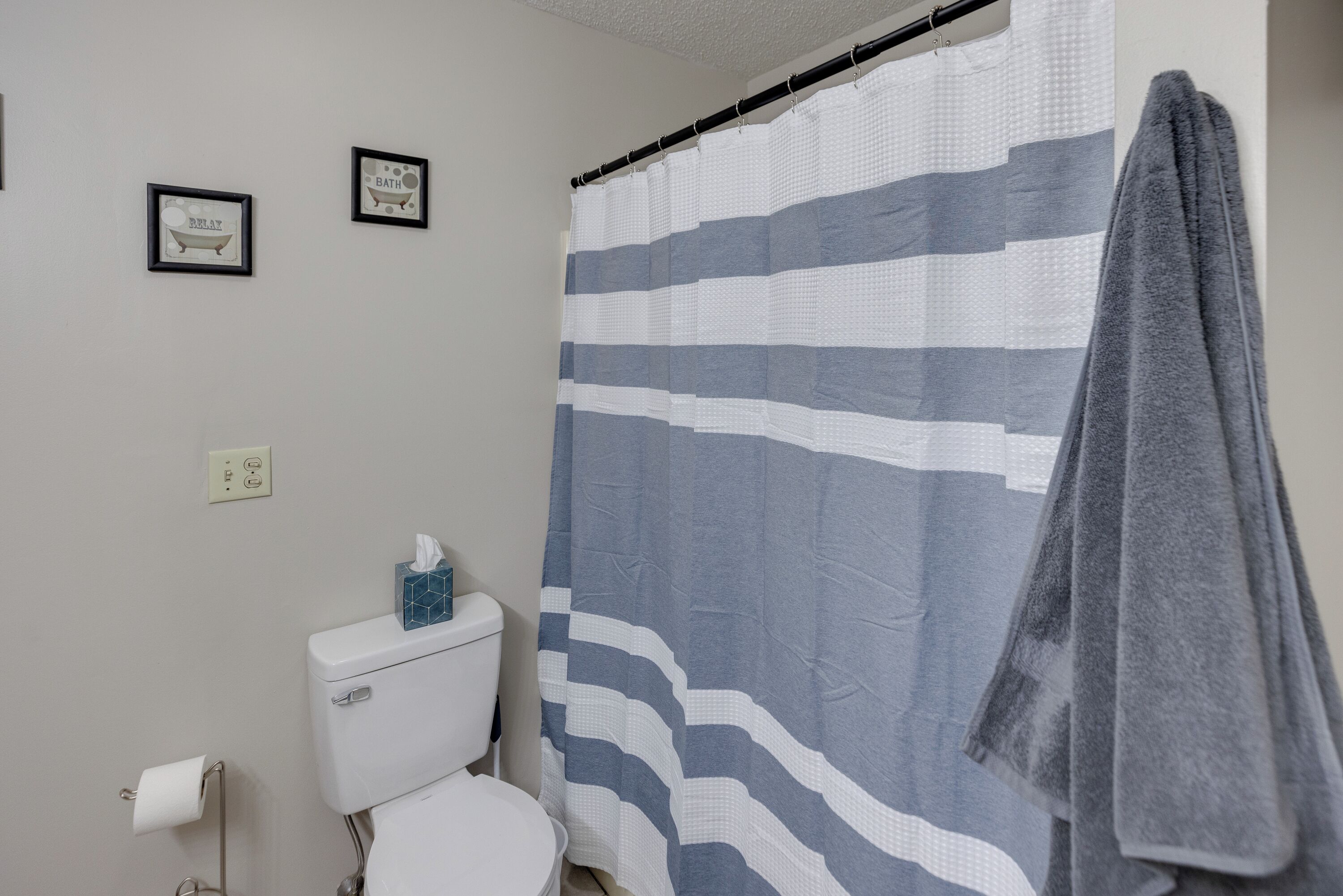 Un baño con cortina de ducha a rayas, un inodoro y dos cuadros en la pared.