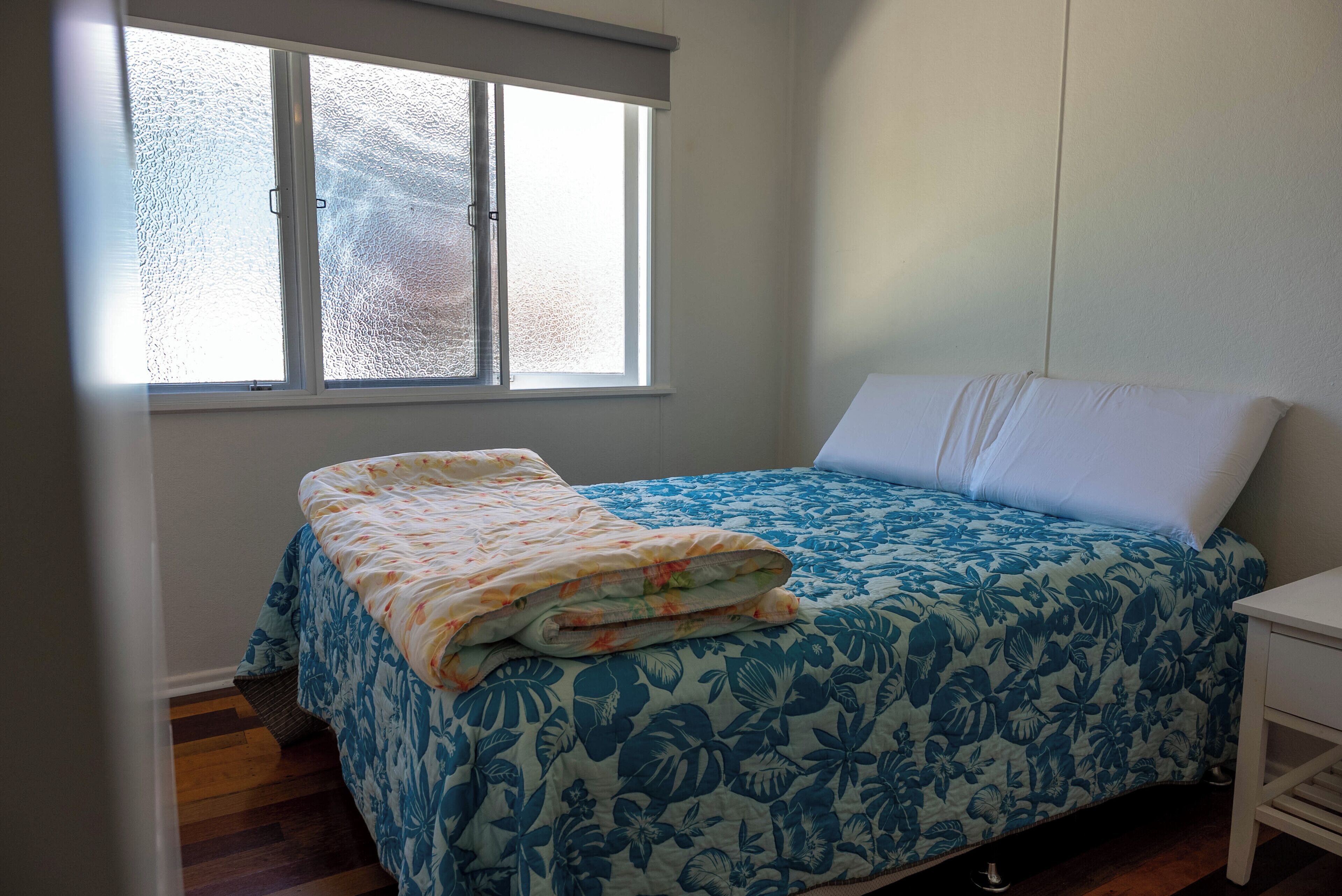 Een slaapkamer met een bed, een raam en een nachtkastje.