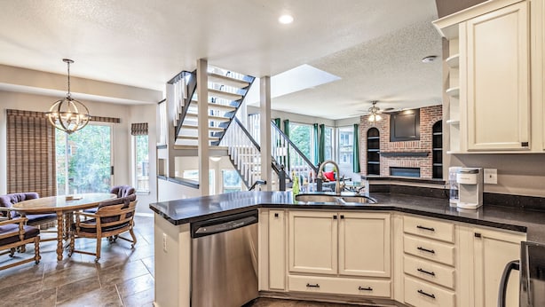A modern kitchen with a dishwasher, a dining area with a wooden table and chairs, and a staircase leading to another level. - Spacious Centennial 4BR with Pool Table and Patio (Centennial)