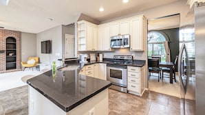 A modern kitchen with white cabinets, a black countertop, stainless steel appliances, and a dining area with a table and chairs. - Spacious Centennial 4BR with Pool Table and Patio (Centennial)