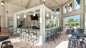 A spacious outdoor bar area with multiple seating options, including bar stools and chairs, and a flat-screen TV mounted on the wall. - Condo 2bd/2bh 15 min from parks Storey Lake (Kissimmee)