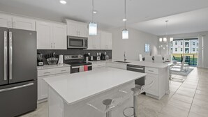 A modern kitchen with white cabinetry, stainless steel appliances, and a large island with bar stools. - Condo 2bd/2bh 15 min from parks Storey Lake (Kissimmee)