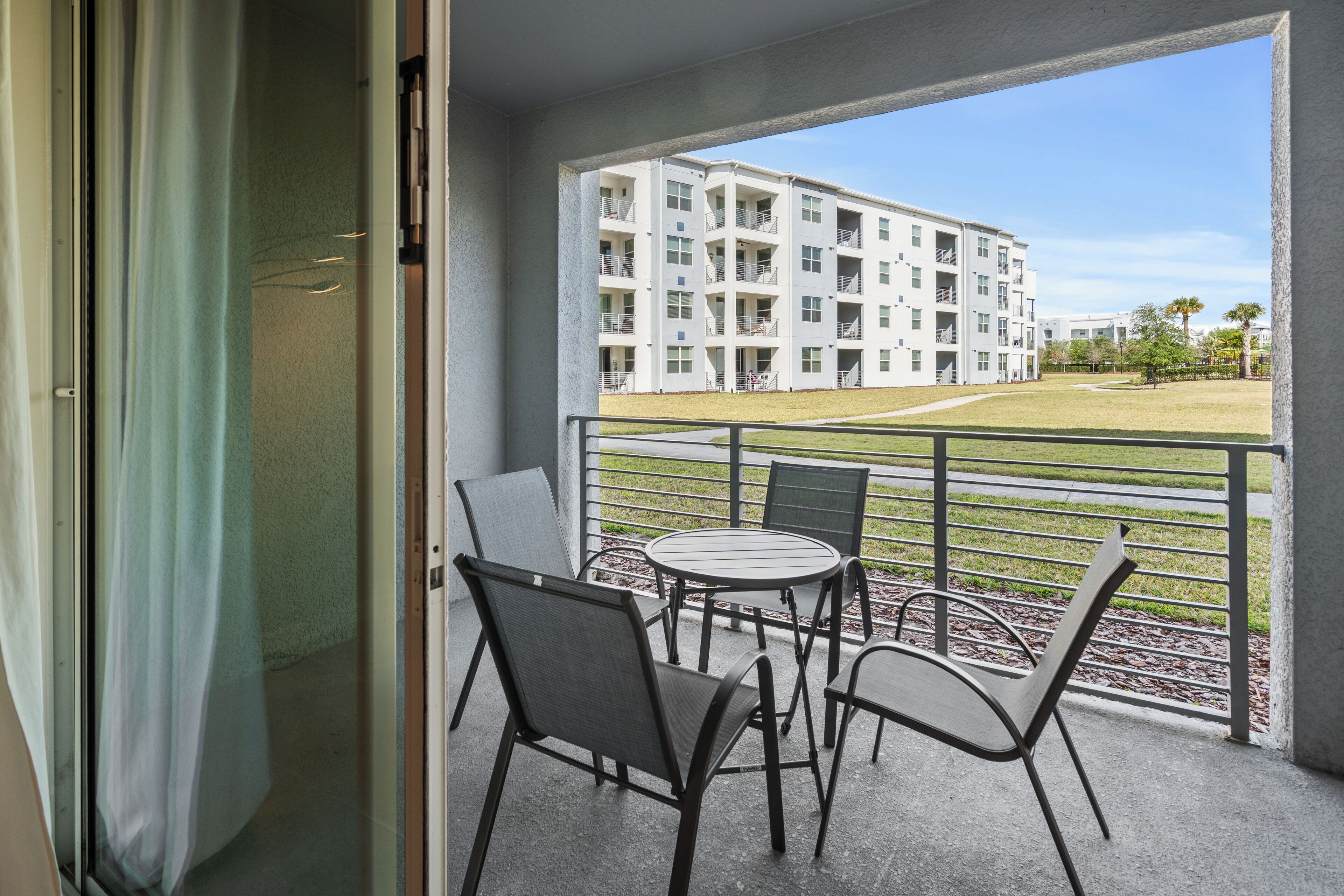 Un balcon donnant sur un immeuble à plusieurs étages, une pelouse et une rambarde en métal.