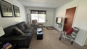 Una sala de estar con sofá, sillón, mesa de centro y televisor sobre un mueble.