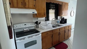 Una cocina compacta con armarios de madera, estufa blanca, lavamanos y ventana con persianas.