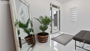 Ein modernes Interieur mit einem großen Spiegel, zwei Topfpflanzen, einer Bank und einer Glastür, die nach draußen führt.