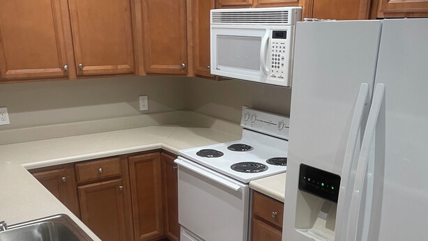 Une cuisine avec des meubles de rangement en bois, une cuisinière blanche, un four à micro-ondes et un réfrigérateur.