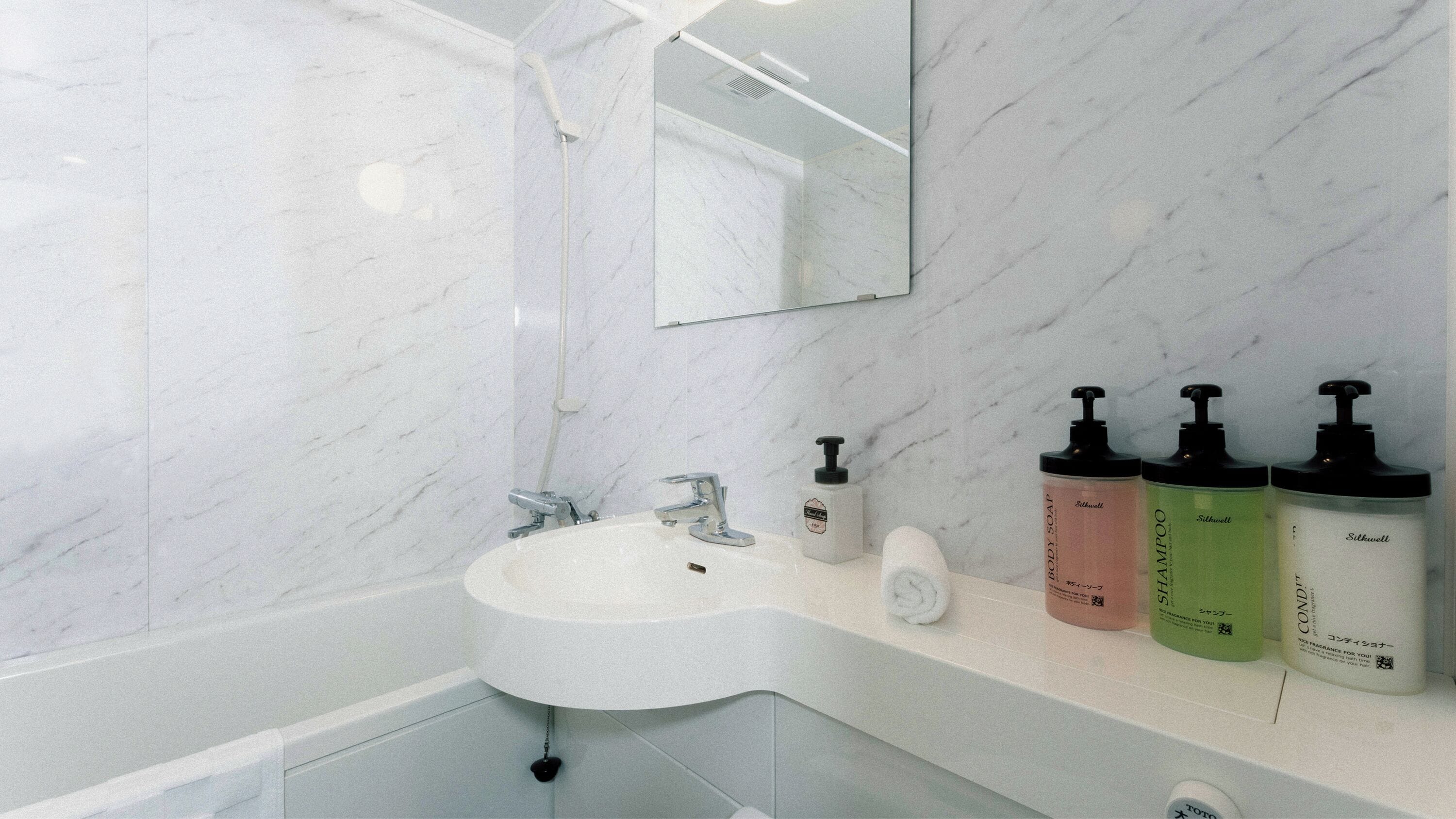 A bathroom with a white sink, a mirror, and three toiletry bottles on the counter.
