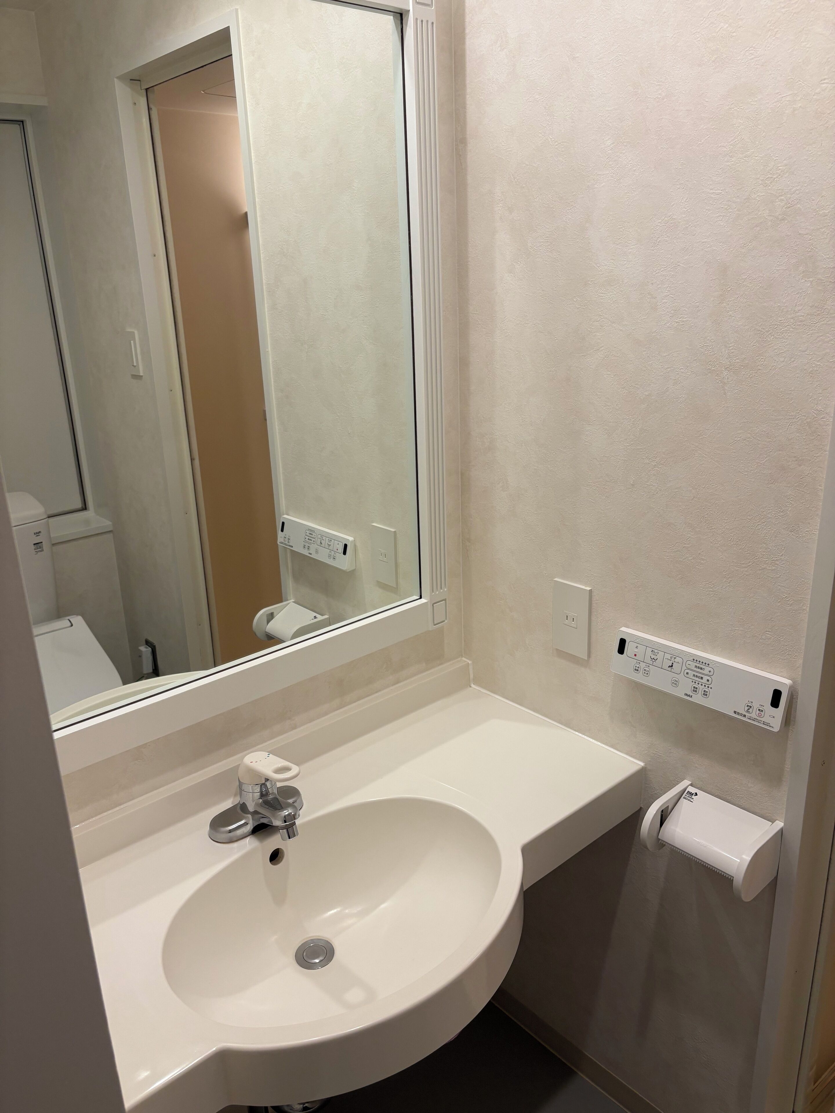 A bathroom with a white sink, a mirror, and a towel dispenser.