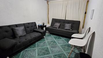 Uma sala de estar pequena com dois sofás pretos, uma poltrona branca e um chão com padrão verde.