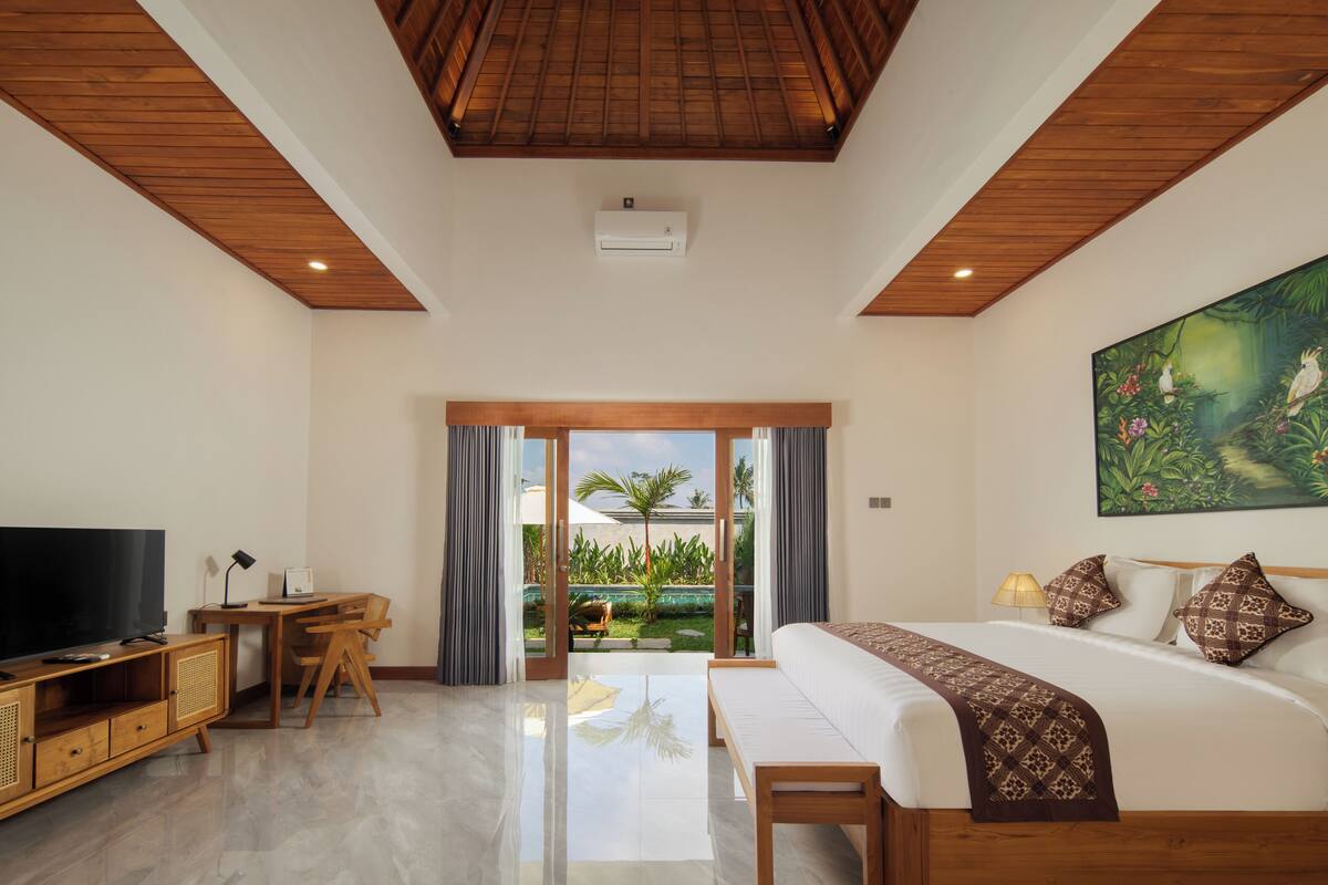 A bedroom with a large bed, a TV, a desk, and a view of a garden through glass doors.