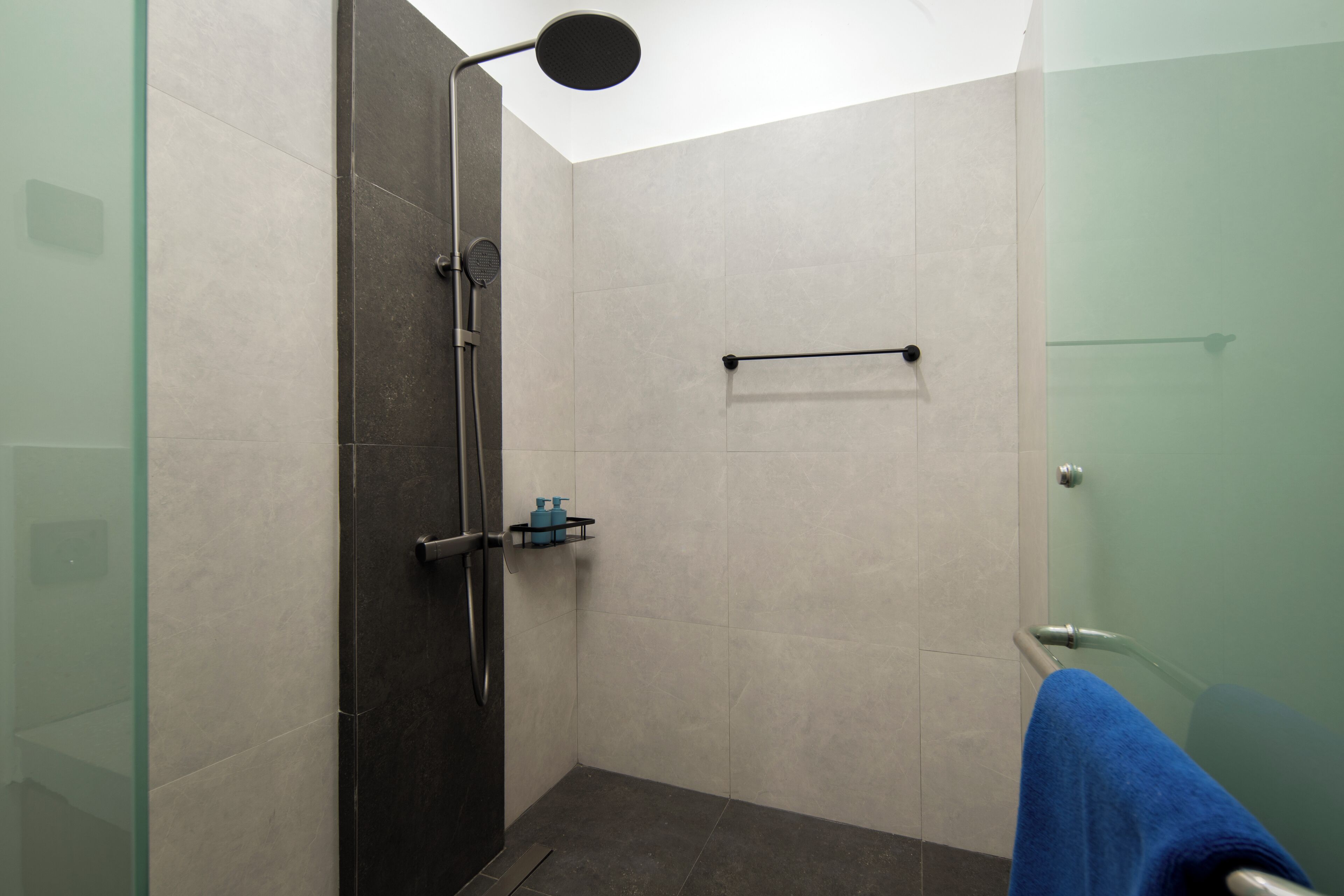 Ein modernes Badezimmer mit Duschkabine aus Glas, einem Handtuchhalter und einer kleinen Ablage mit Toilettenartikeln.