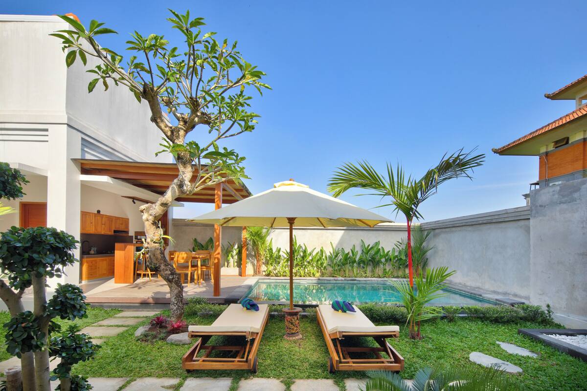 A modern outdoor pool area with lounge chairs, a dining set, and a large umbrella.