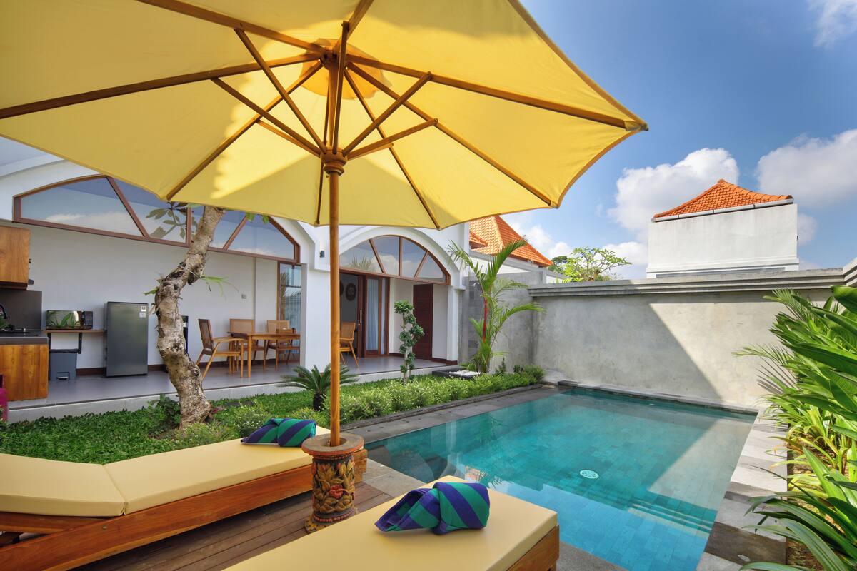 A pool area with a yellow umbrella, wooden lounge chairs, and a small garden.