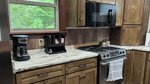 A kitchen with wooden cabinets, a stainless steel stove, a microwave, and a coffee maker. - Quiet, relaxing, Guest House with large porch on Cagle Mountain in Dunlap, Tn. (Dunlap)