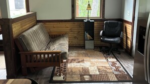 A compact living space with a wooden bench, a desk, a chair, a clock, a window with a view of trees, and a ceiling fan. - Quiet, relaxing, Guest House with large porch on Cagle Mountain in Dunlap, Tn. (Dunlap)