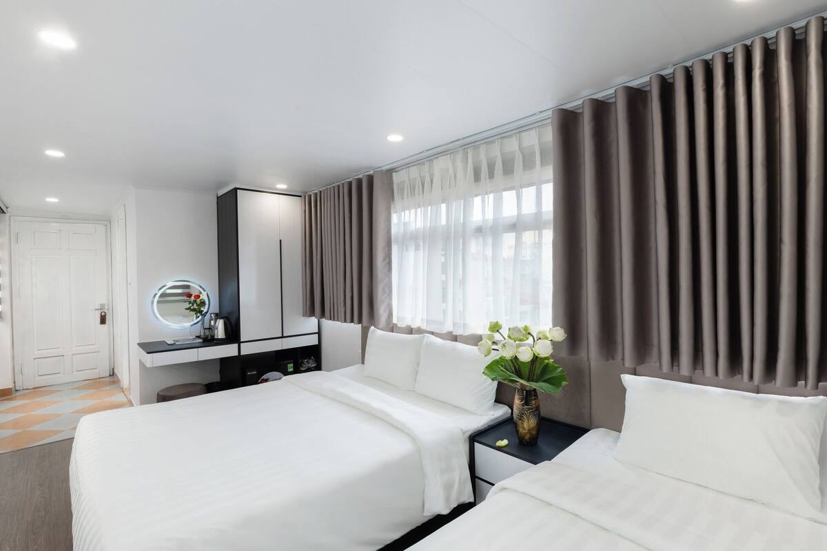 A hotel room with two beds, a vanity with a mirror, and a window with curtains.