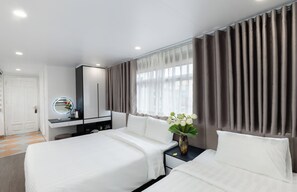 Quarto de hotel com duas camas, uma toucador com espelho e uma janela com cortinas.