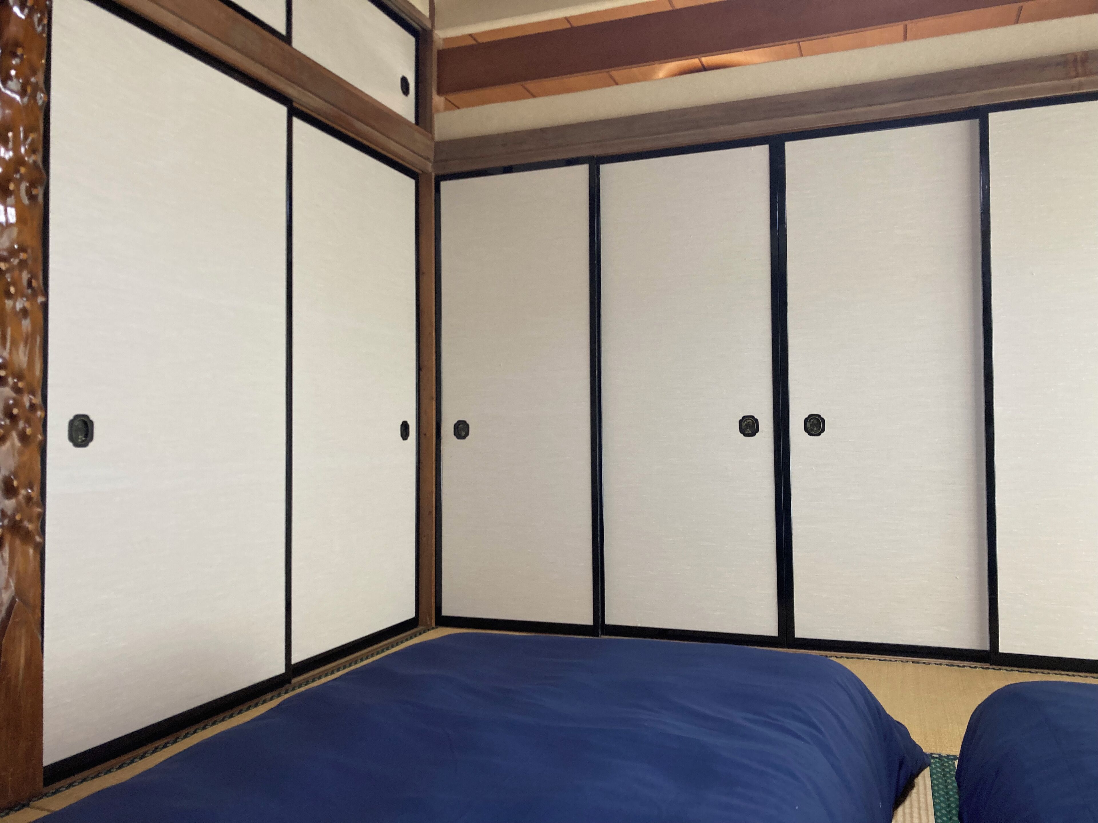 A traditional Japanese room with tatami flooring, a low wooden ceiling, and sliding doors.