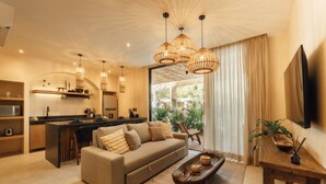 Ein modernes Wohnzimmer mit Sofa, Couchtisch und Essbereich. Im Hintergrund befindet sich eine Küche, ein großes Fenster mit Vorhängen und ein an der Wand befestigter Fernseher.