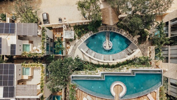 Ein Pool auf dem Dach mit kreisförmigem Design, umgeben von üppiger Vegetation und modernen Gebäuden.