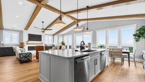 Una cocina amplia con una isla grande, vigas de madera, luces colgantes y vistas al exterior.