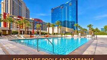 A hotel pool area with a clear blue pool, lounge chairs, and palm trees.