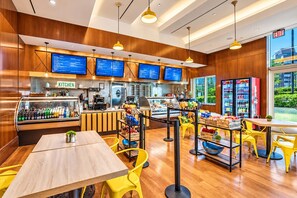 A restaurant interior with wooden paneling, yellow chairs, a counter with a coffee machine, and a menu display.