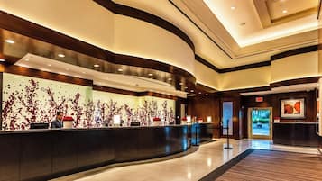A modern hotel lobby with a curved reception desk, a large wall with a red floral pattern, and a framed artwork on the wall.