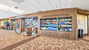 Un hall d’hôtel doté d’un kiosque intitulé « ESSENTIELS », où l’on trouve des en-cas et des boissons, ainsi qu’une poubelle et un tapis à motifs bois.