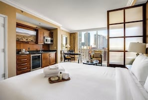 Habitación de hotel con una cama grande, kitchenette, comedor y vistas a la ciudad.