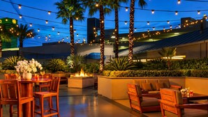 An outdoor patio with wooden furniture, a fire feature, and string lights against a night sky.