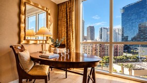 Une chambre d’hôtel avec une grande fenêtre, une table à manger ronde, une chaise, une lampe et un vase avec une plante.