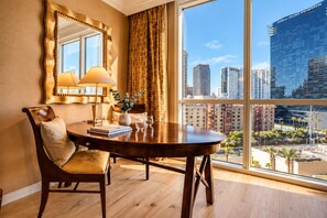 A hotel room with a large window, a round dining table, a chair, a lamp, and a vase with a plant.