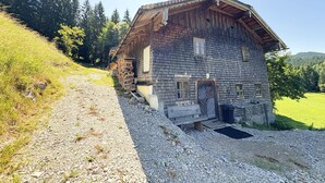Ein rustikales Holzhaus mit einem geneigten Dach, einer kleinen Veranda und einem Schotterweg.