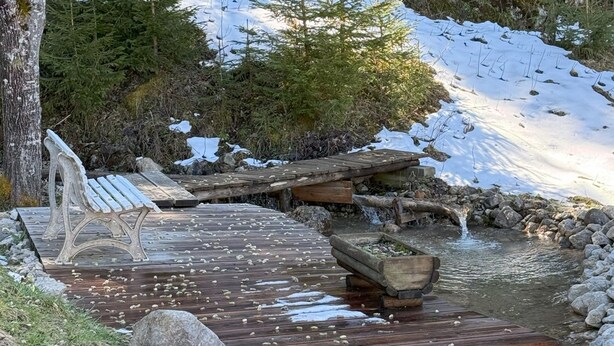 Eine Holzterrasse mit Bänken und einem kleinen Teich, umgeben von Steinen und Schnee.