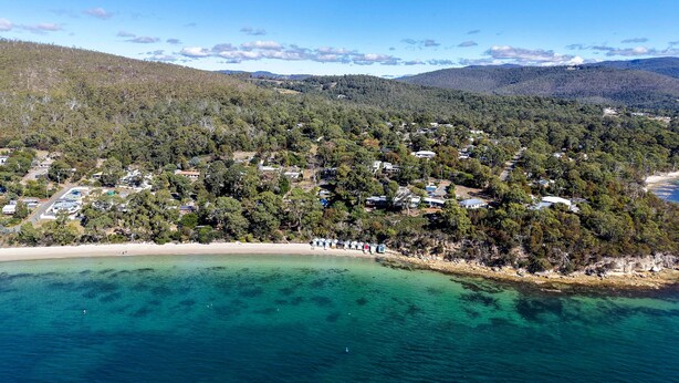 An aerial view of a coastal area with a beach, dense forest, and scattered buildings. - Coningham Beach House (Coningham)