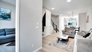 A modern living room with a sofa, a coffee table, and a dining area with a chair and table. - 6BDR Family Retreat | Remote Work Ready-2 | Kitchens-2 | Lake Access | Games (Calgary)