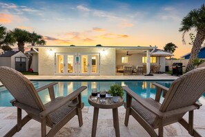 A poolside area with wicker chairs, a small table with drinks, and a building with a covered patio.