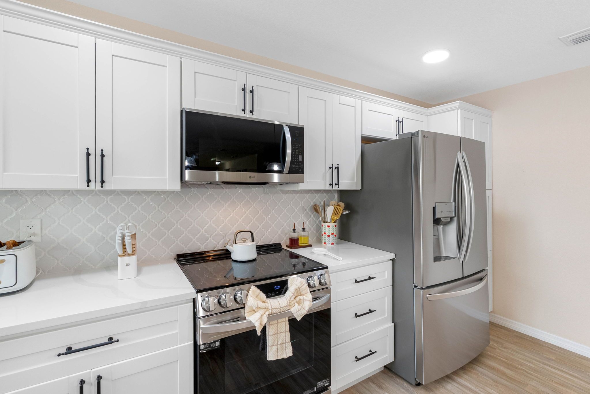 A modern kitchen with white cabinets, a stainless steel microwave, a double oven, and a large refrigerator.