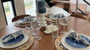 Una mesa de comedor preparada con platos, vasos y una vela, con una escalera y una planta al fondo.