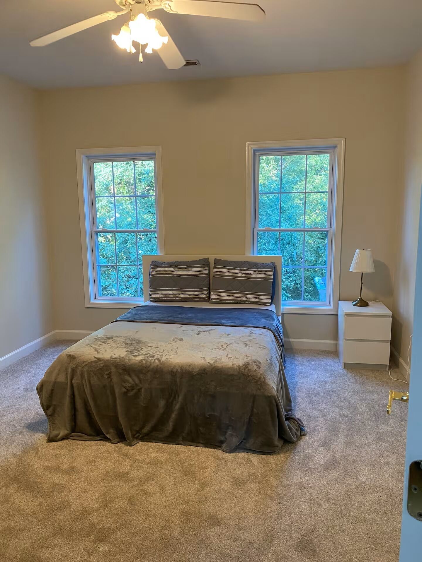 A bedroom with a bed, two windows, a nightstand, and a ceiling fan.